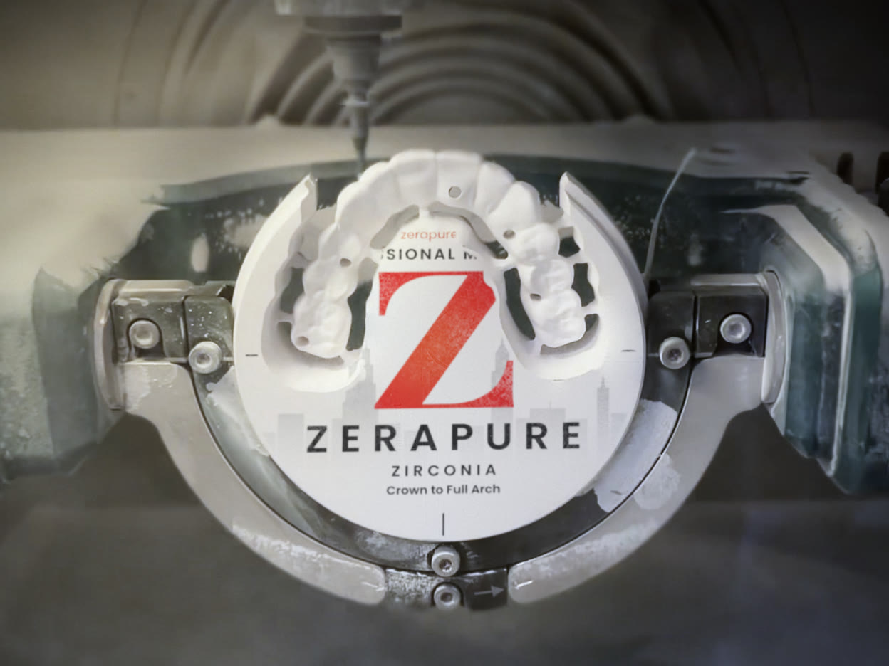 Wide view of a Zerapure zirconia disc held in the mill, with a milled full-arch restoration